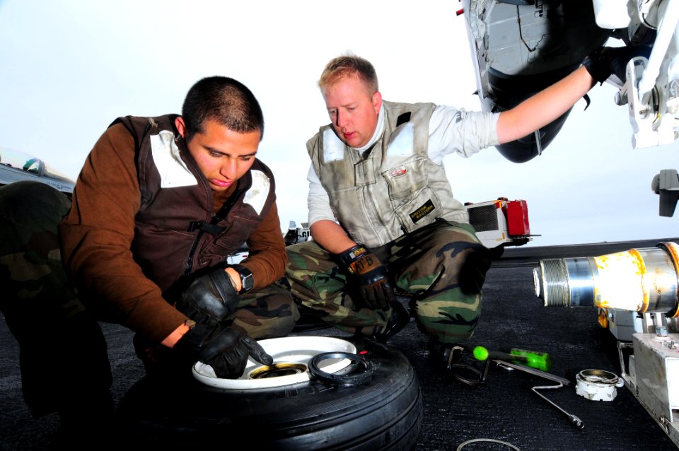 US Navy 090528-N-3946H-061 Aviation Electronics Technician 1st Class Dan Becker teaches Aviation Electronics Technician Airman Erick Avalos how to change the tires of an F-A-18C Hornet