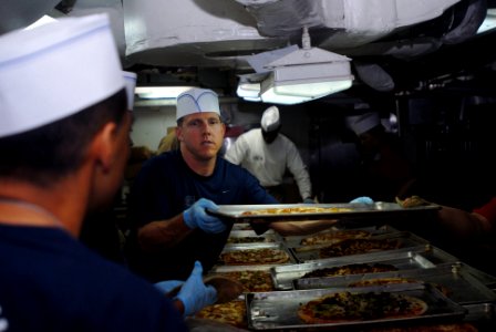 US Navy 090529-N-9132C-127 Senior Chief Electronics Technician James Ritch passes a pizza down the line to serve in the galley aboard the aircraft carrier USS Ronald Reagan (CVN 76)