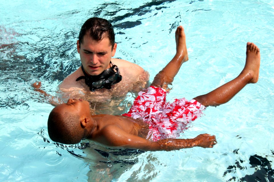 US Navy 090608-N-8110K-035 Navy Diver 2nd Class Bobby Demay, assigned to Mobile Diving and Salvage Unit 2 based at Navy Amphibious Base Little Creek, Va., teaches a child how to float