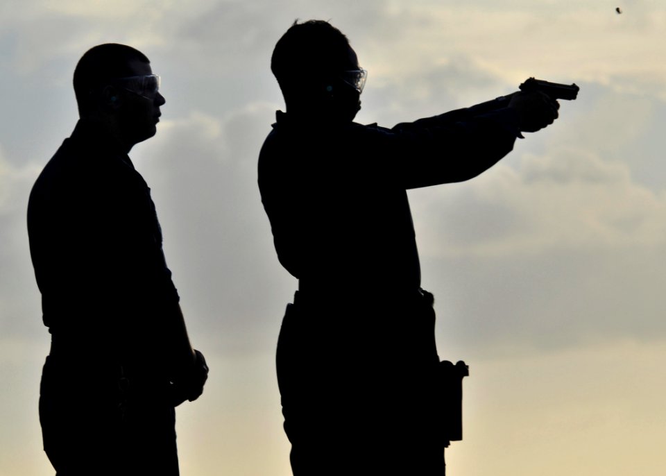 US Navy 090618-N-2638R-003 Gunner's Mate 2nd Class Anthony Robe watches as Personnel Specialist 1st Class Carrie Alexander, from Chicago, fires a 9mm pistol during pistol qualifications