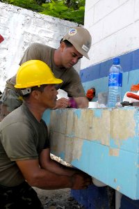 US Navy 090625-F-7923S-074 Utilitiesman 2nd Class Carlos Monserrat helps Cabo Santos Jouel Portillo install new pipes for a sink during the renovation of a bathroom at the Club de Leons School photo