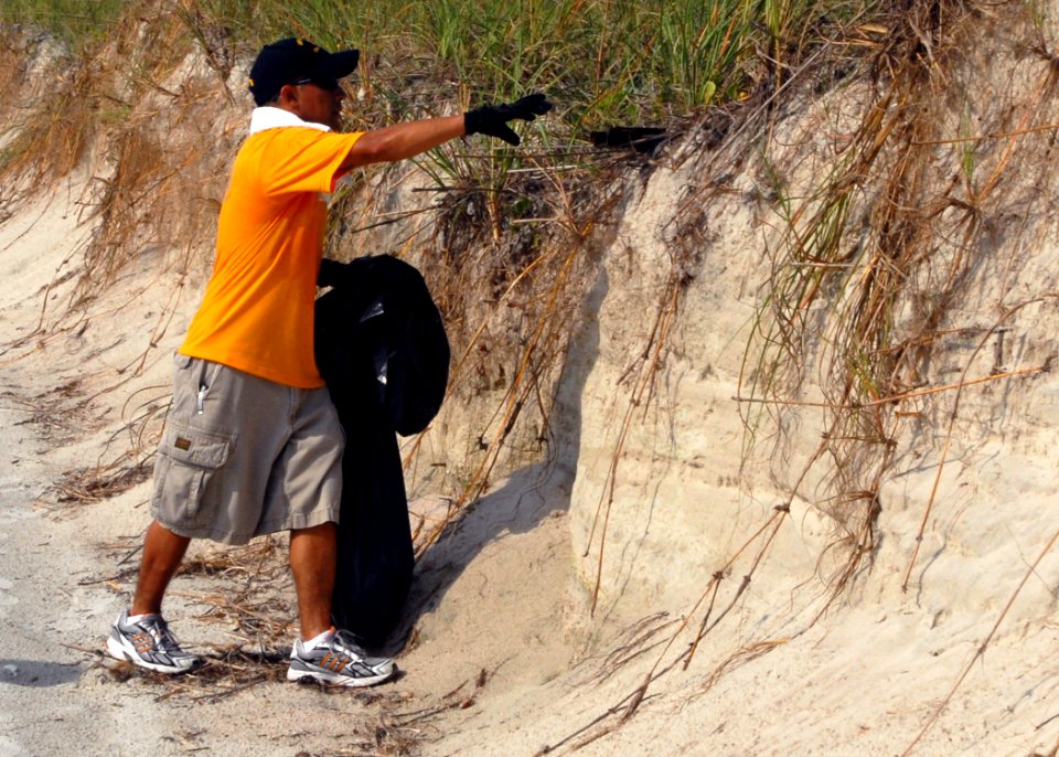US Navy 090716-N-0486G-003 A Sailor assigned to the guided-missile destroyer USS The Sullivans (DDG 68) reaches for a piece of trash during the mid-summer beachfront clean up