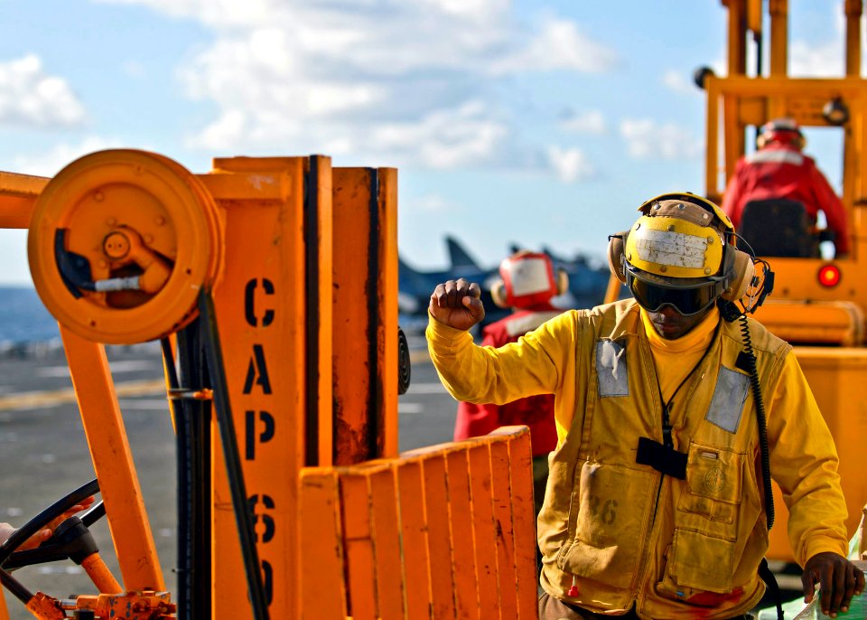 US Navy 090718-N-9950J-400 Aviation Boatswain's Mate (Handling) Airman Jessie Washington directs a forklift on the flight deck of the forward-deployed amphibious assault ship USS Essex (LHD 2) during a vertical replenishment