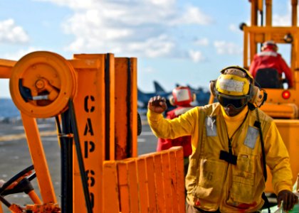 US Navy 090718-N-9950J-400 Aviation Boatswain's Mate (Handling) Airman Jessie Washington directs a forklift on the flight deck of the forward-deployed amphibious assault ship USS Essex (LHD 2) during a vertical replenishment