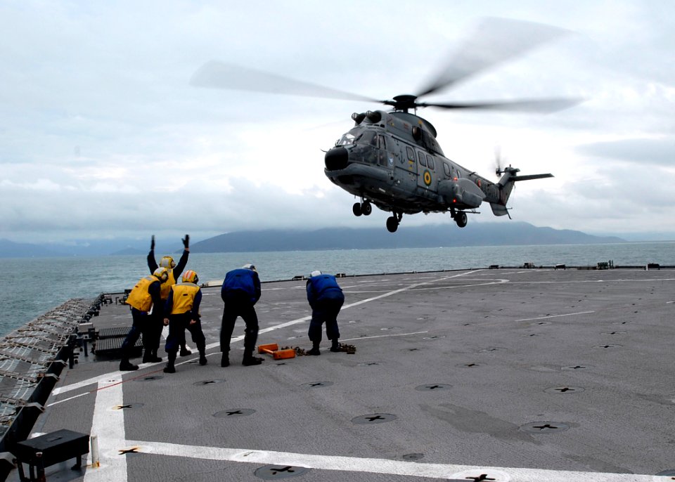 US Navy 090725-N-0924R-020 Boatswain's Mate 3rd Class Andrew Tabin waves a Brazilian Super Puma helicopter off the flight deck of the amphibious dock landing ship USS Oak Hill (LSD 51) during deck landing qualifications