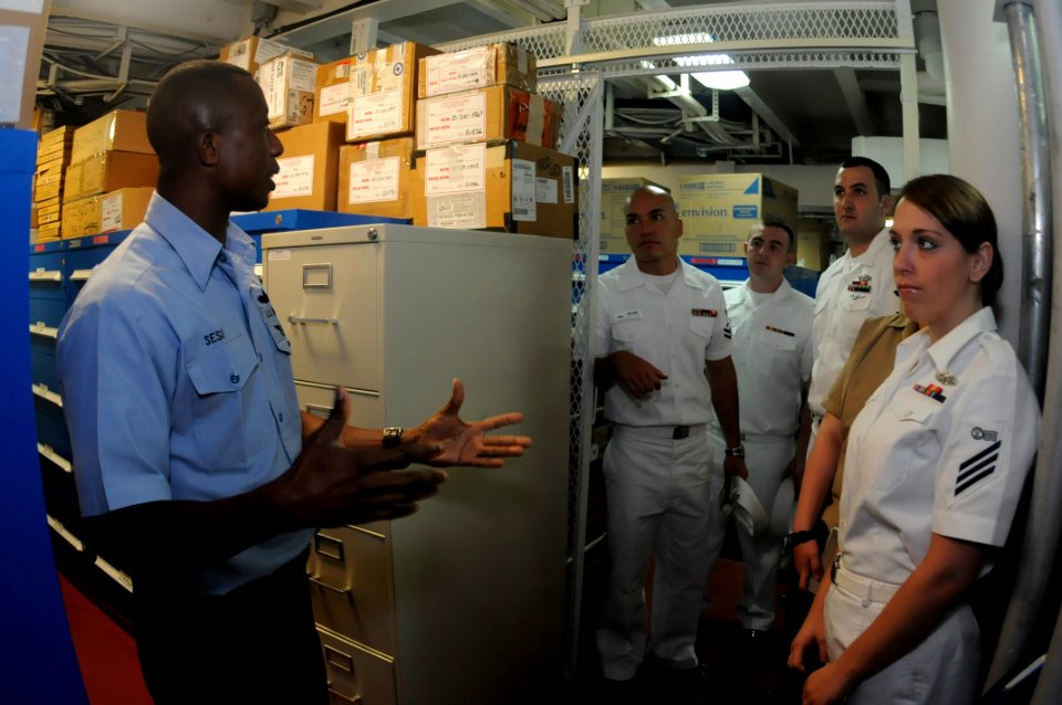 US Navy 090731-N-7478G-020 Storekeeper 1st Class Yayah Sesay, assigned to the amphibious command ship USS Blue Ridge (LCC 19), gives a tour of the stock control office
