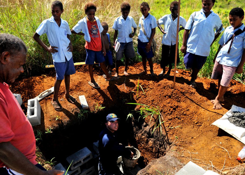 US Navy 090807-N-2638R-004 Children from the Ariliguo Primary School watch as Gas Turbine System Technician (Electrical) 2nd Class Kristofer Regalado builds a retaining wall for a septic drain field