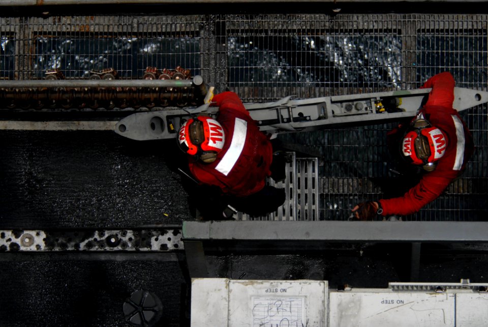 US Navy 090801-N-9132C-267 Two Aviation Ordnancemen assigned to the Fighting Redcocks of Strike Fighter Squadron (VFA) 22 carry a bomb rack onto the flight deck of the aircraft carrier USS Ronald Reagan (CVN 76)