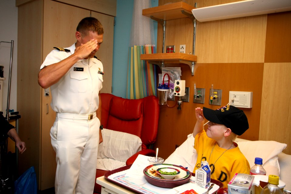 US Navy 090902-N-3271W-236 Lt. Cmdr. Andrew Baldwin, M.D., a Navy undersea medical officer, shows a young patient at Nationwide Children's Hospital how to salute after presenting him with a Navy ball cap