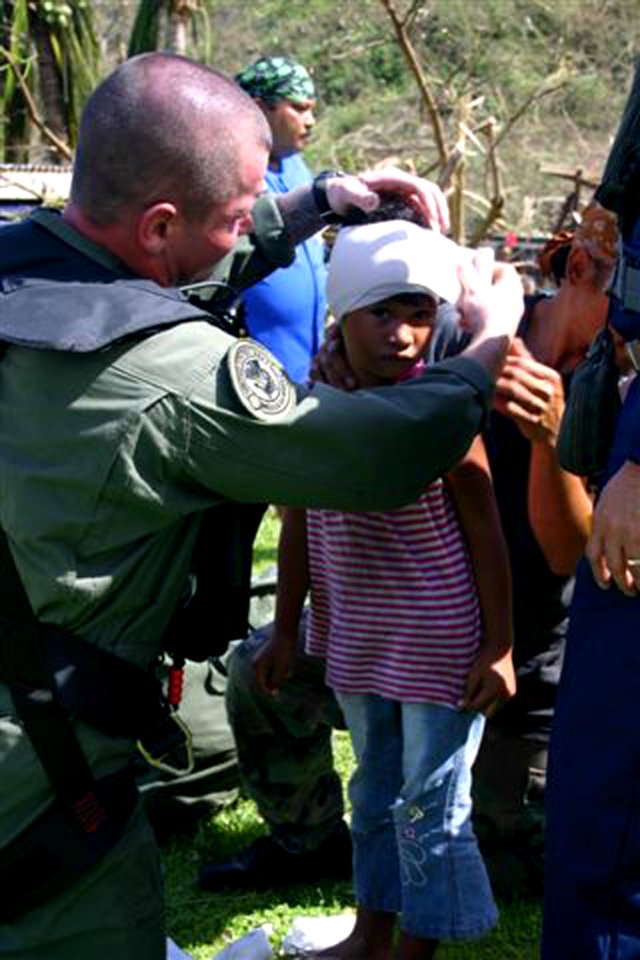 US Navy 090917-N-xxxxx-004 A Sailor assigned to Helicopter Sea Combat Squadron (HSC) 25 provides basic first aid to a young girl on the island of Alamagan following the aftermath of Super Typhoon