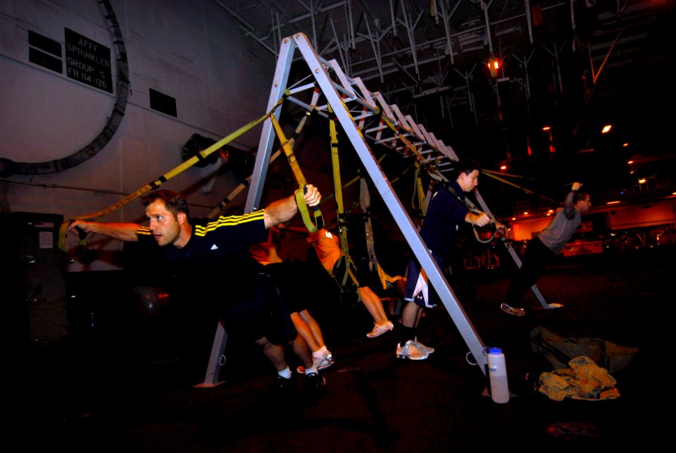 US Navy 090919-N-2475A-100 Fitness Director Joshua Burkhard leads a Total Resistance Exercise (TRX) session in the hangar bay aboard the aircraft carrier USS John C. Stennis (CVN 74)