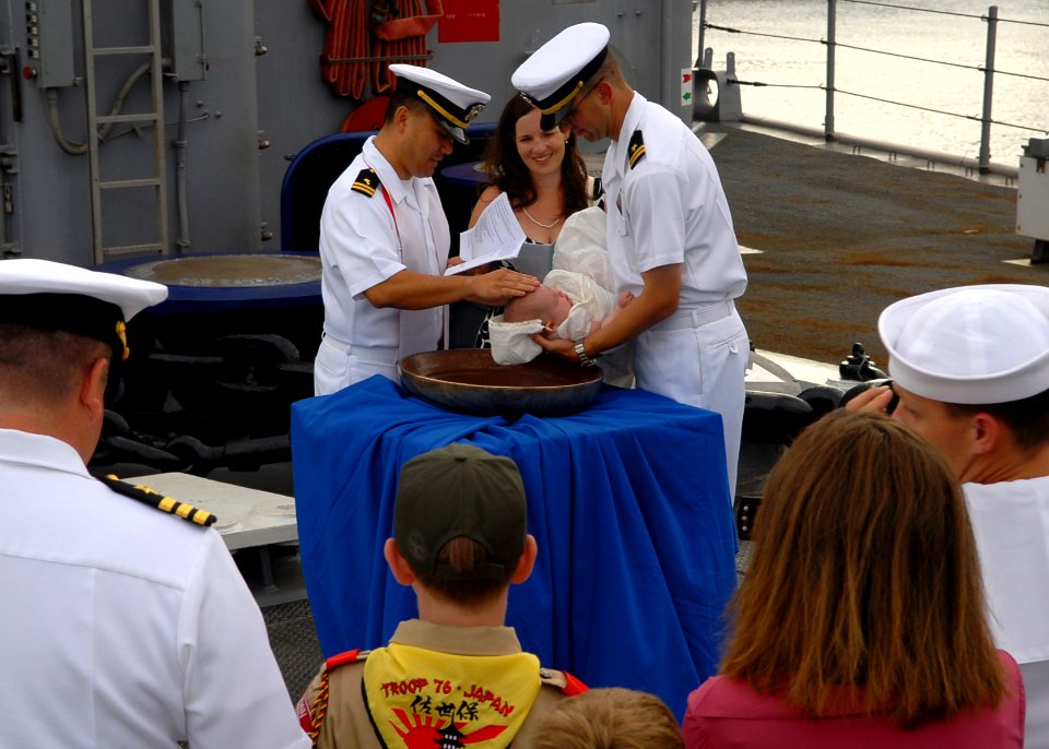 US Navy 090917-N-6692A-047 Lt. John Madea holds his daughter as she is baptized with holy water from the ship's bell of the amphibious dock landing ship USS Tortuga (LSD 46)