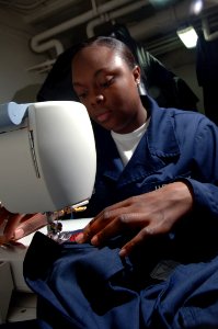 US Navy 090923-N-4053P-002 Ship's Serviceman Seaman Champagnee Travis sews a set of crows to a uniform in the tailor shop of the aircraft carrier USS Nimitz (CVN 68)