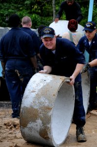 US Navy 090924-N-4995K-131 Aviation Ordnanceman Airman Thomas Curley, assigned to the aircraft carrier USS Ronald Reagan (CVN 76), rolls a cement ring for a sewage tank during work on a Habitat for Humanity house in Phuket, Tha