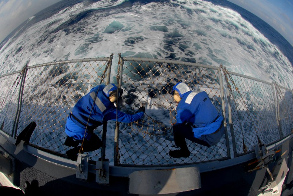 US Navy 090930-N-1688B-140 Sailors aboard the guided-missile destroyer USS Cole (DDG 67) take advantage of a break during flight quarters to repair a hole in the safety netting around the flight deck
