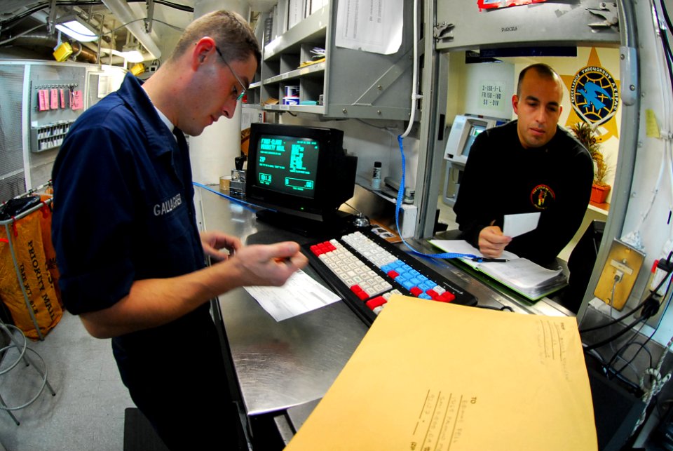 US Navy 090928-N-2918M-103 Postal Clerk Seaman Apprentice Noel Gallagher assists Chief Sonar Technician Armando Berajas with mail in the post office aboard the aircraft carrier USS Nimitz (CVN 68)