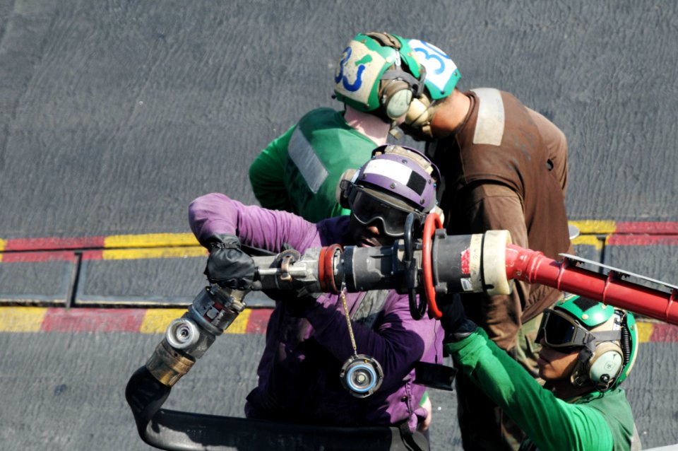 US Navy 091006-N-3038W-082 Sailors assigned to the air department of the aircraft carrier USS Nimitz (CVN 68) attache a fuel line to the in-flight refuel port on an F-A-18C Hornet