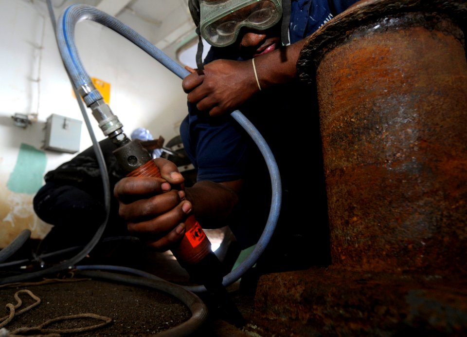 US Navy 091009-N-7280V-131 Seaman Darrell Moore removes rust with a needle gun in a mooring station aboard the amphibious command ship USS Blue Ridge (LCC 19)