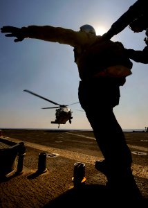 US Navy 091008-N-5345W-086 Boatswain's Mate 1st Class Courtney Bacchas is braced by Seaman Michale Sturdevant while signaling the pilot of an MH-60S Sea Hawk helicopter assigned to the Sea Knights of Helicopter Sea Combat Squad