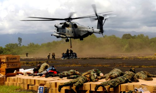 US Navy 091012-N-7130B-146 Military and relief agency personnel use their bodyweight to prevent relief supplies from being swept away by the downdraft created by a CH-53E Super Stallion helicopter