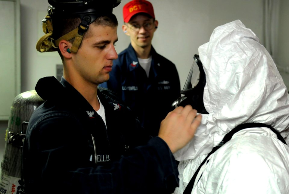 US Navy 091017-N-7280V-180 Damage Controlman 3rd Class Travis Mueller adjusts the advanced chemical protective garment of Information Systems Technician 3rd Class Jonetta McCoy during a toxic gas drill aboard the amphibious com