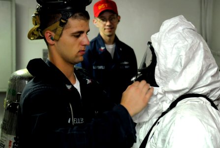 US Navy 091017-N-7280V-180 Damage Controlman 3rd Class Travis Mueller adjusts the advanced chemical protective garment of Information Systems Technician 3rd Class Jonetta McCoy during a toxic gas drill aboard the amphibious com