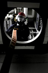 US Navy 091022-N-7280V-323 Mass Communication Specialist 2nd Class Josh Cassatt, a Repair Locker 2 investigator, lowers a fire hose to the boundary man during a major fuel oil leak drill aboard the amphibious command ship USS B