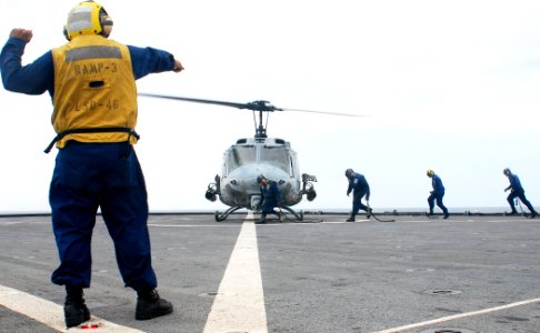 US Navy 091030-N-6692A-061 Boatswain's Mate 2nd Class Carlos Gonzales signals the pilot while Sailors approach to secure a Marine Corps UH-1N Huey helicopter aboard the amphibious dock landing ship USS Tortuga (LSD 46)