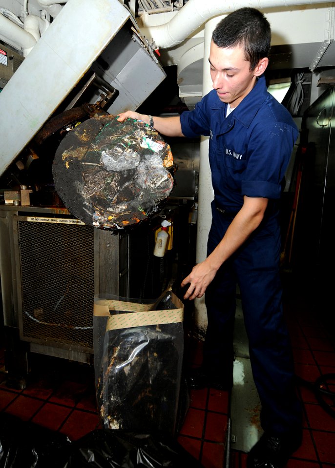 US Navy 091107-N-6233H-003 Hull Technician Fireman Ryan Konkol removes melted plastic from a compressed melting unit at the mid-ship pulper