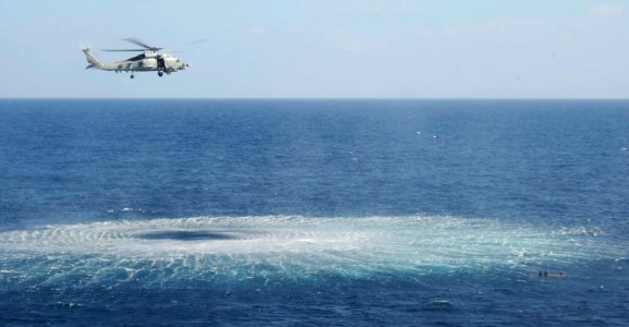 US Navy 091117-N-9500T-531 An SH-60B Sea Hawk helicopter hovers near three men clinging to a piece of wood