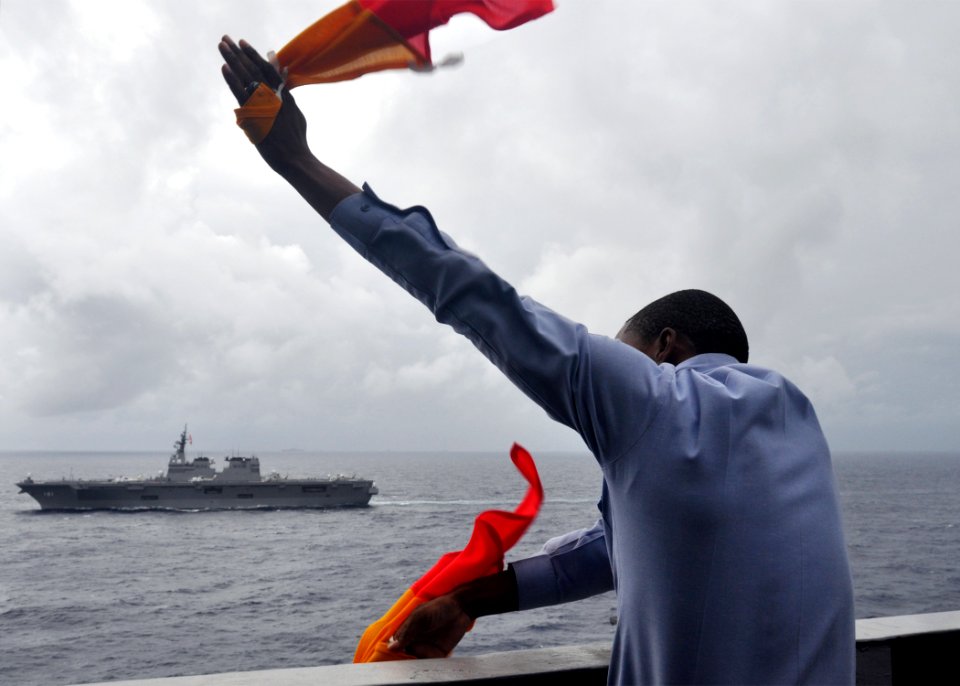 US Navy 091117-N-2013O-030 Quarter Master 3rd Class Alexander Davis sends semaphore signals from the aircraft carrier USS George Washington (CVN 73) to the Japan Maritime Self-Defense Force helicopter destroyer JS Hyuga (DDH 18