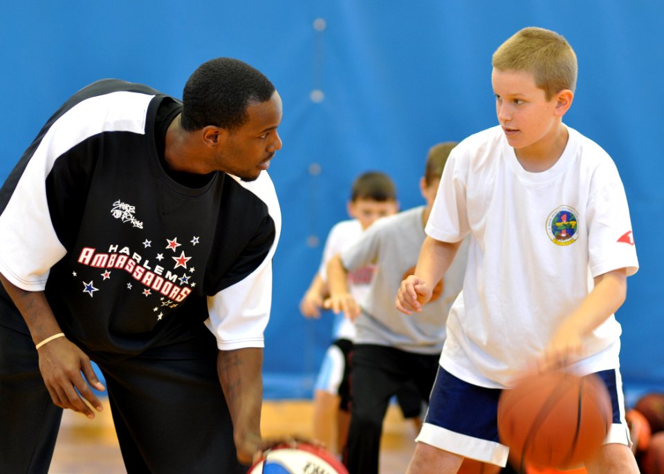 US Navy 091206-N-2013O-023 Sam Givens, a player for the Harlem Ambassadors basketball team, demonstrates proper dribbling techniques to a boy during a basketball camp sponsored by Yokosuka's Morale, Welfare and Recreation Youth