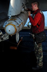 US Navy 091207-N-3038W-539 Aviation Ordnanceman Airman Trevor Fleischman, assigned to the Black Aces of Strike Fighter Squadron (VFA) 41, attaches a bomb fuse cable to a bomb on an F-A-18F Super Hornet