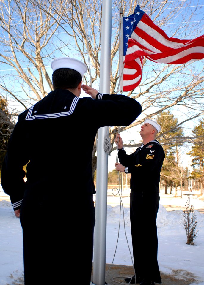 US Navy 091223-N-9898L-006 Aviation Electronics Technician 2nd Class Alejandro Benavides renders honors as Aviation Structural Mechanic 1st Class Andrew Johnson lowers the American flag outside of the Navy Operational Support C
