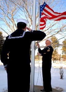 US Navy 091223-N-9898L-006 Aviation Electronics Technician 2nd Class Alejandro Benavides renders honors as Aviation Structural Mechanic 1st Class Andrew Johnson lowers the American flag outside of the Navy Operational Support C