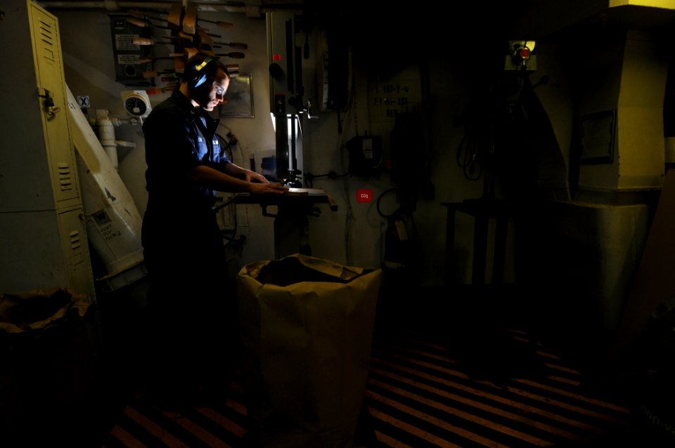 US Navy 100104-N-1688B-018 Hull Technician 3rd Class Elijah Coe uses a band saw to cut out wooden plaques