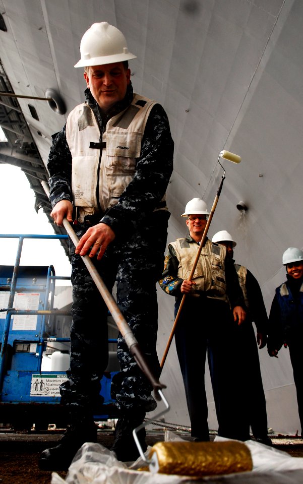 US Navy 100111-N-9928E-063 Capt. Joseph Kuzmick, commanding officer of the aircraft carrier USS John C. Stennis, dips a roller into a paint pan during a golden anchor painting ceremony