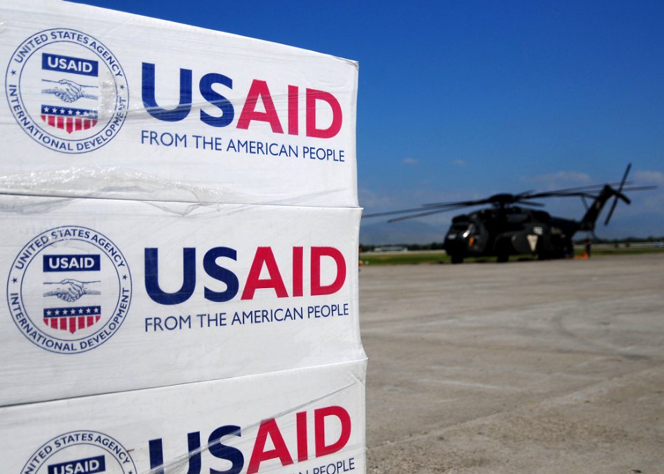 US Navy 100117-N-6247V-083 Pallets of food, water and supplies sit on the flight line at the airport as a MH-53E helicopter from Helicopter Mine Countermeasures Squadron 14 awaits to be on loaded with supplies