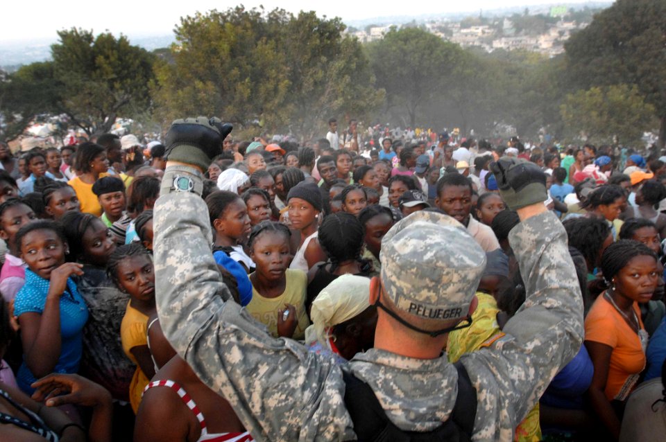 US Navy 100119-D-1852B-277 Army Pfc. Jonathan Pflueger holds his hands above a crowd of women to try to get them to sit down at a humanitarian aid distribution point