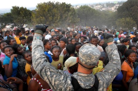 US Navy 100119-D-1852B-277 Army Pfc. Jonathan Pflueger holds his hands above a crowd of women to try to get them to sit down at a humanitarian aid distribution point