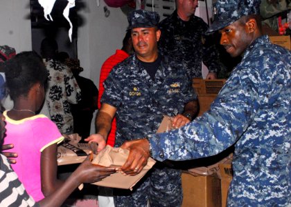US Navy 100119-N-5244H-040 Cmdr. George Doyon, left, commanding officer of the amphibious dock landing ship USS Carter Hall (LSD 50), and Sailors assigned to Carter Hall distribute meals-ready-to-eat