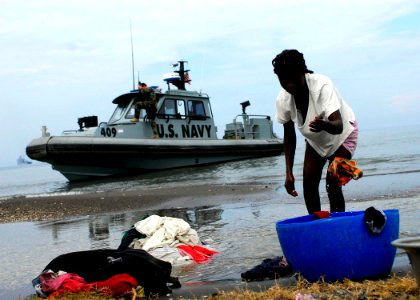 US Navy 100119-N-5244H-003 A Haitian girl washes laundry by the shore as Sailors on an assault craft boat stand watch over the arrival of heavy equipment photo