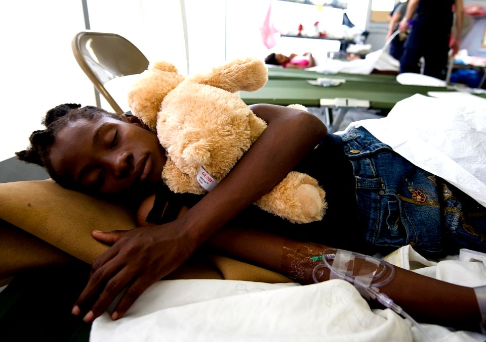 US Navy 100119-N-6266K-158 A young Haitian girl holds her teddy bear while she sleeps after receiving medical treatment at Gheskio Field Hospital