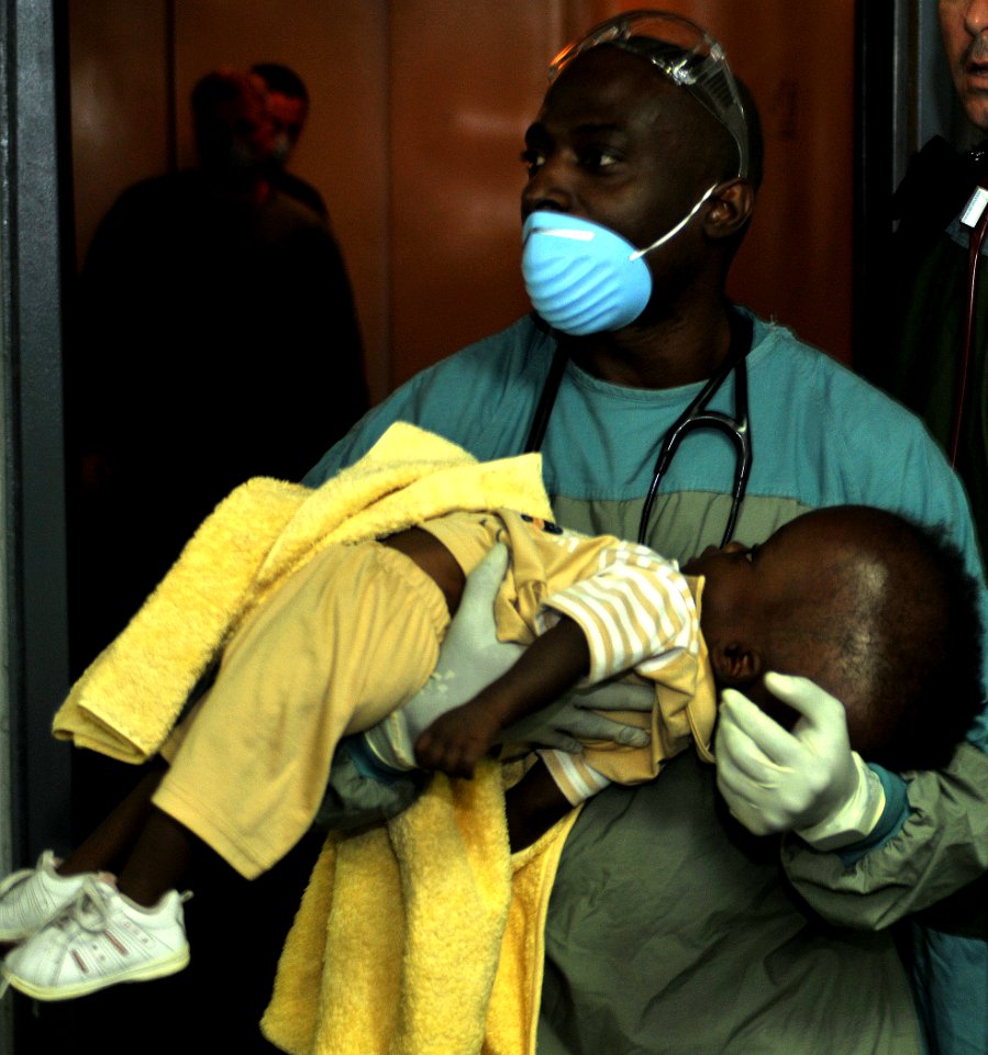 US Navy 100120-N-1831S-055 Senior Chief Hospital Corpsman Huben Phillips carries a Haitian infant into the medical triage area aboard USS Bataan (LHD 5)