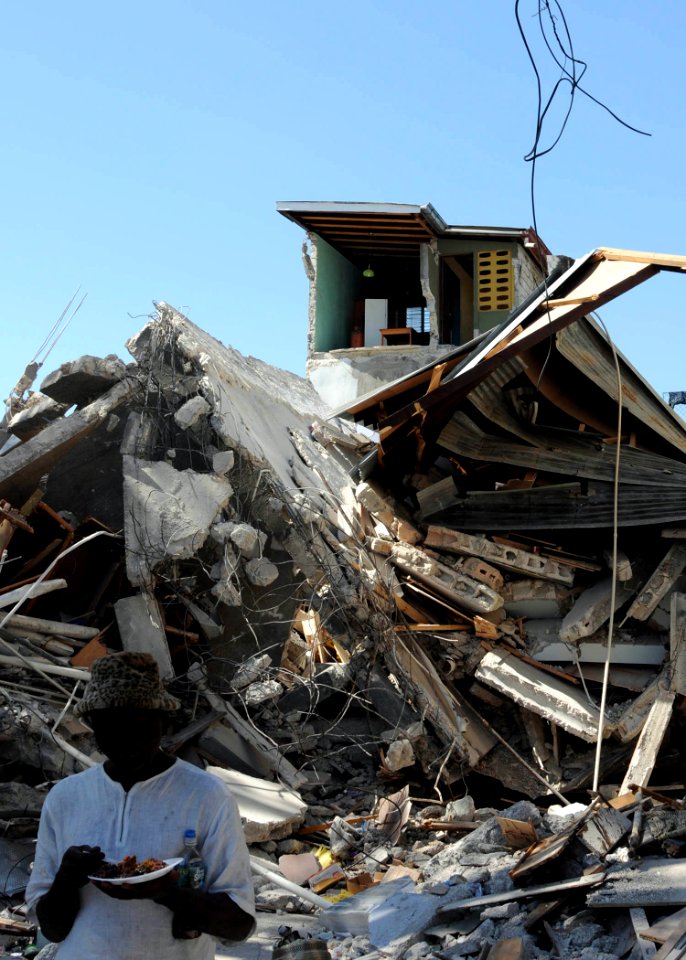US Navy 100121-N-6410J-242 A Haitian man eats a meal in front of a building that was destroyed during the 7.0 magnitude earthquake in the Caribbean nation of Haiti on Jan. 12, 2010