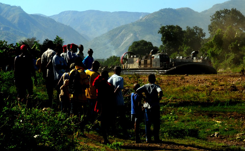 US Navy 100122-N-7508R-020 Haitians watch as a landing craft air cushion (LCAC) assigned to Assault Craft Unit (ACU) 4 offloads relief supplies from the multi-purpose amphibious assault ship USS Bataan (LHD 5)
