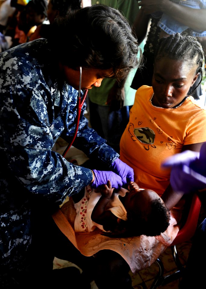 US Navy 100125-N-5345W-263 Hospital Corpsman 1st Class Vilma Bauer, assigned to the amphibious dock landing ship USS Fort McHenry (LSD 43) examines a Haitian infant as her family looks on while seeking treatment