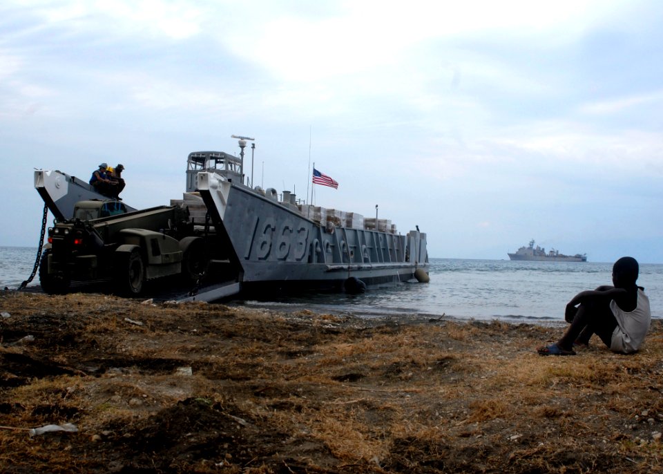 US Navy 100126-N-2000D-394 A Haitian boy watches as Seabees offload pallets of meals-ready-to-eat from Landing Craft Unit (LCU) 1663