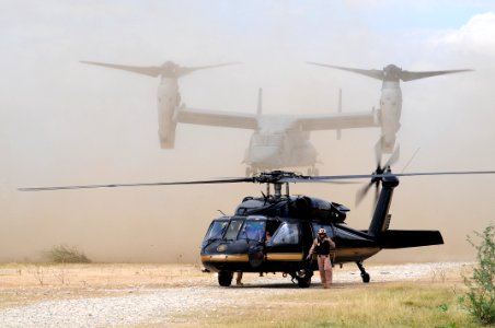 US Navy 100126-N-6247V-171 A U.S. Customs and Border Patrol helicopter awaits passengers as a Navy MV-22 Osprey tilt-rotor aircraft lands in the background near the U.S. Embassy in Port-au-Prince, Haiti
