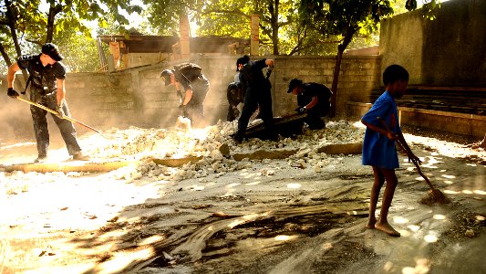 US Navy 100129-N-5345W-089 A young Haitian boy sweeps as Sailors assigned to the multi-purpose amphibious assault ship USS Bataan (LHD 5) clear rubble and debris from an outdoor classroom